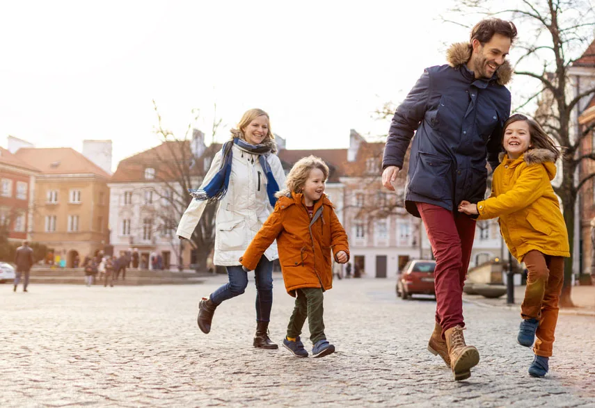 Mamma, pappa och två barn är ute på ett torg och leker tillsammans, iklädda höstjackor.