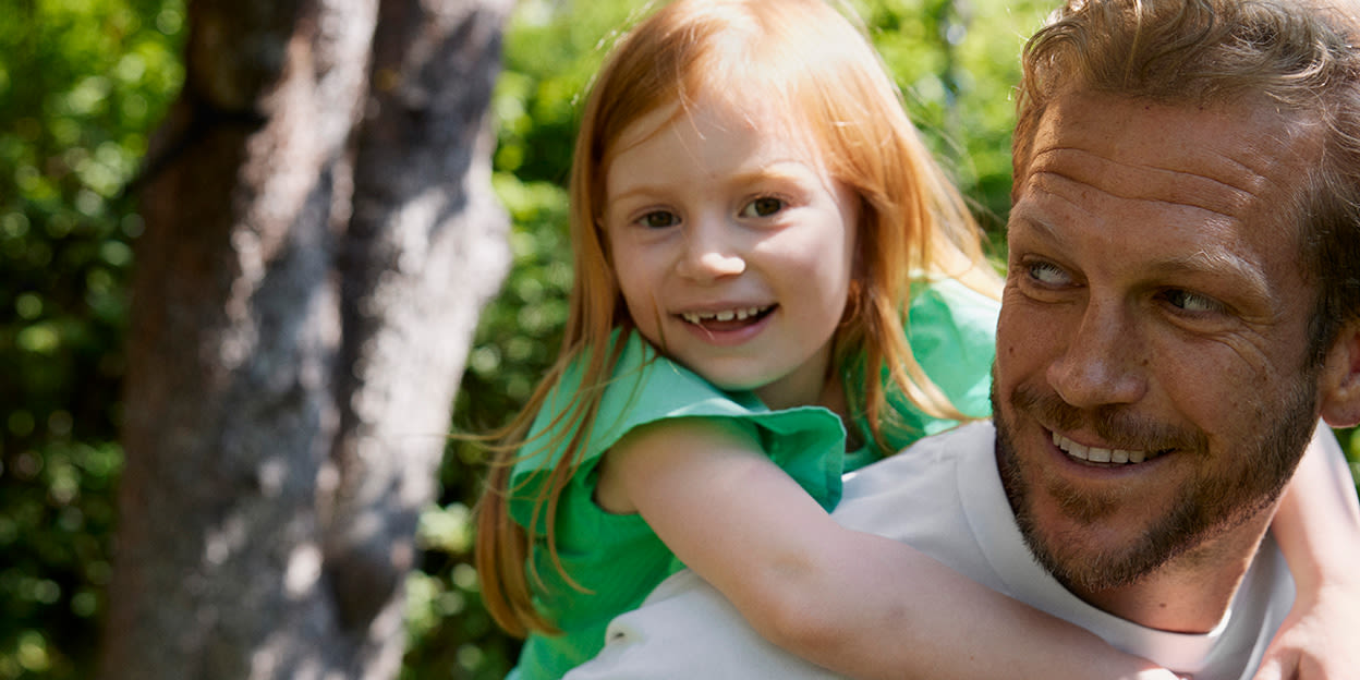 Pappa har sin dotter på ryggen. De är glada och utomhus en sommardag.