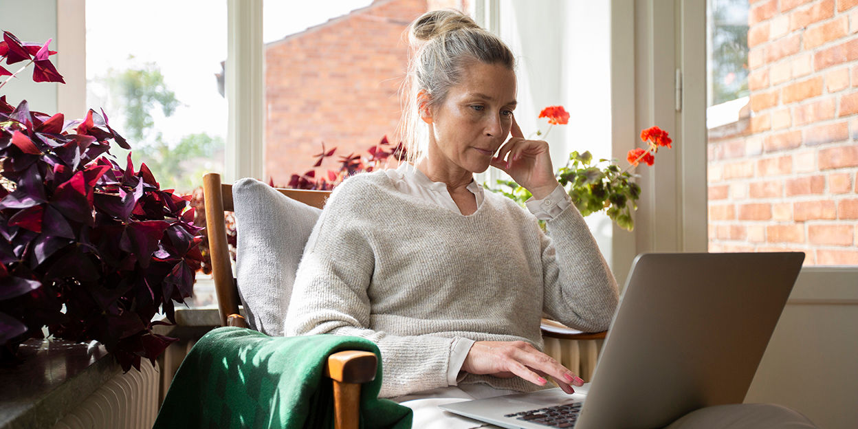 Kvinna sitter i fåtölj och kollar på dator. 