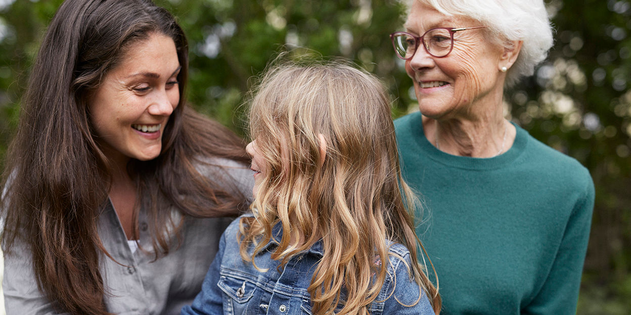 Tre generationer av kvinnor från barn till pensionär som skrattar tillsammans.