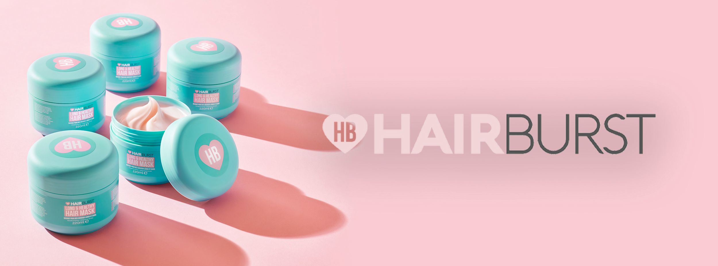 Flera turkosa burkar med Hairburst Long & Healthy Hair Mask står på ett rosa underlag, med Hairburst-logotypen till höger.