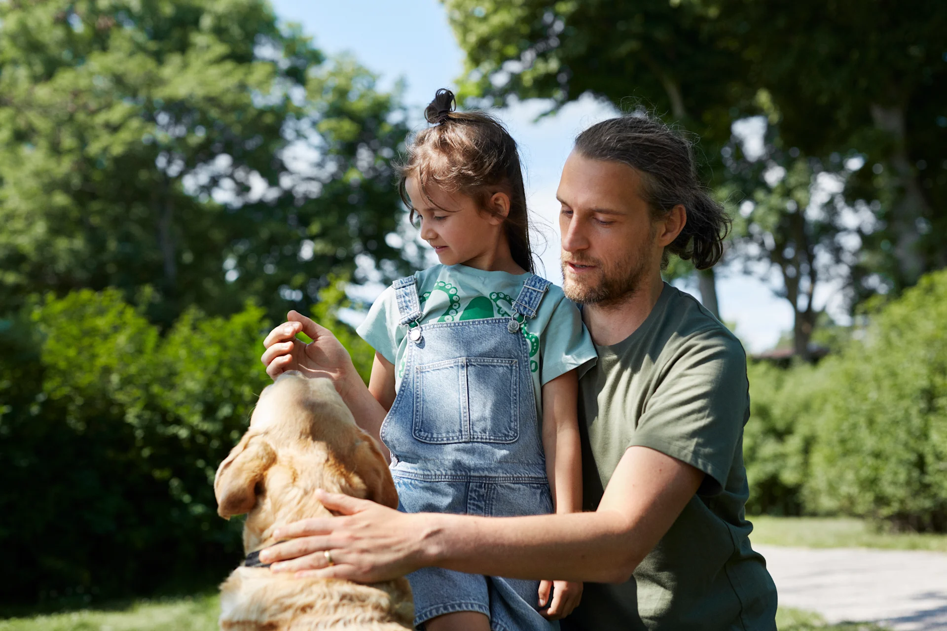 Pappa och dotter leker utomhus med en hund.