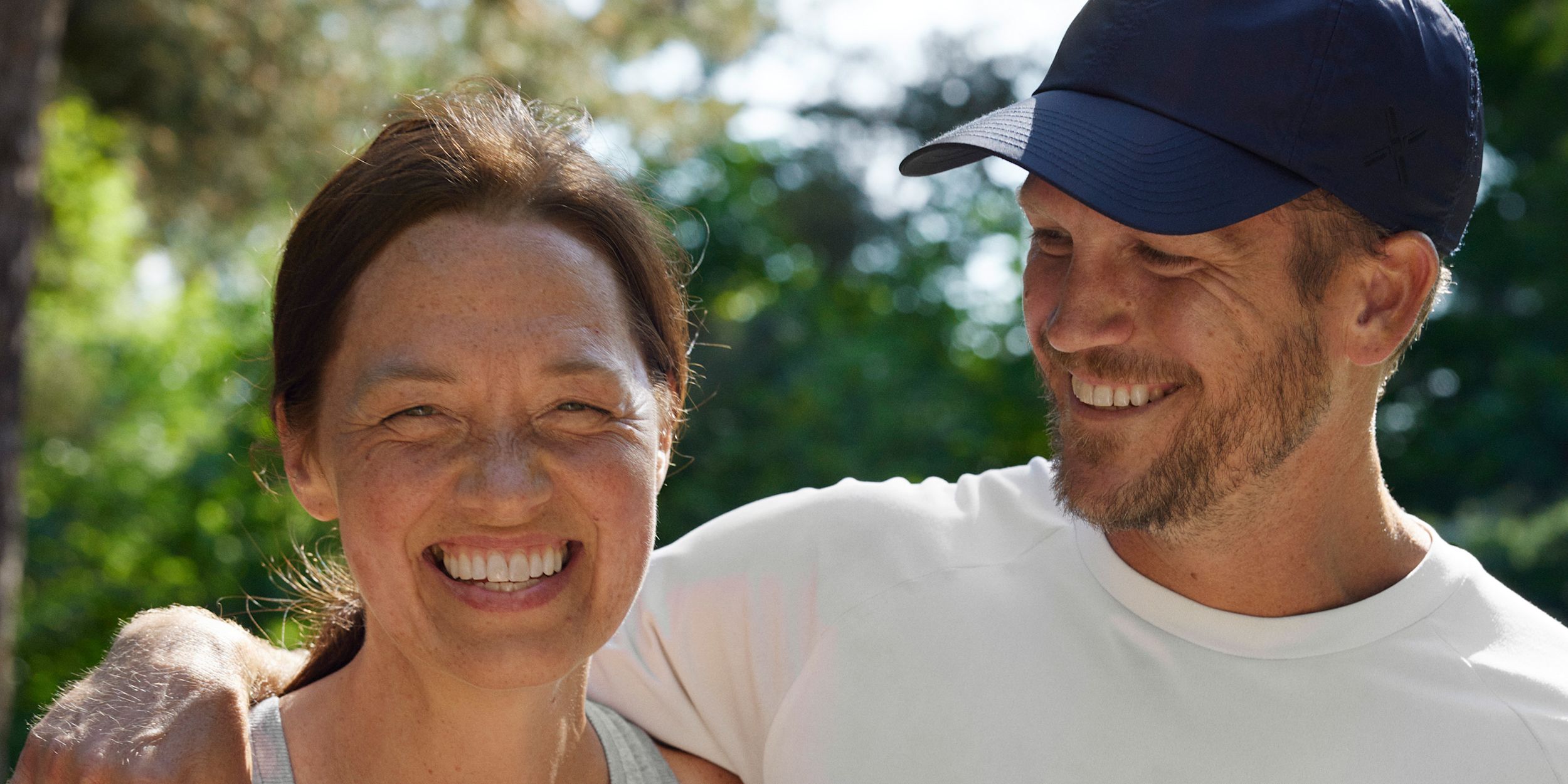 Glad kvinna och man är ute i sommarsolen. Mannen håller om kvinnan om axeln och tittar på henne.