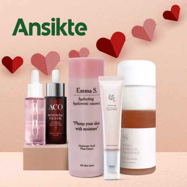 Fem olika ansiktsvårdsprodukter i flaskor och tuber står på en beige yta med en bakgrund av en rosa vägg och en girlang av röda och rosa hjärtan.