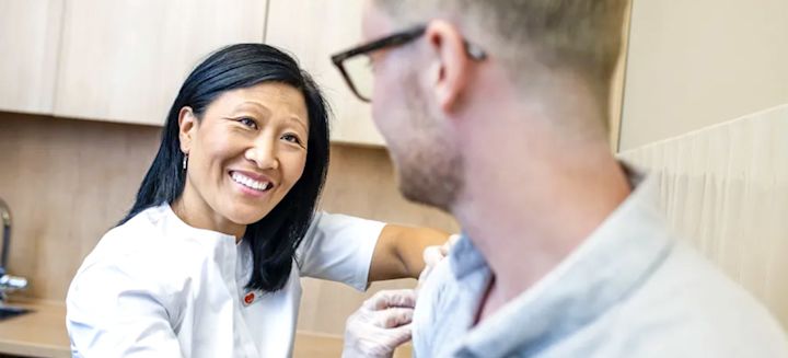 En leende kvinna plåstrar om en manlig patient efter en vaccinationsspruta.