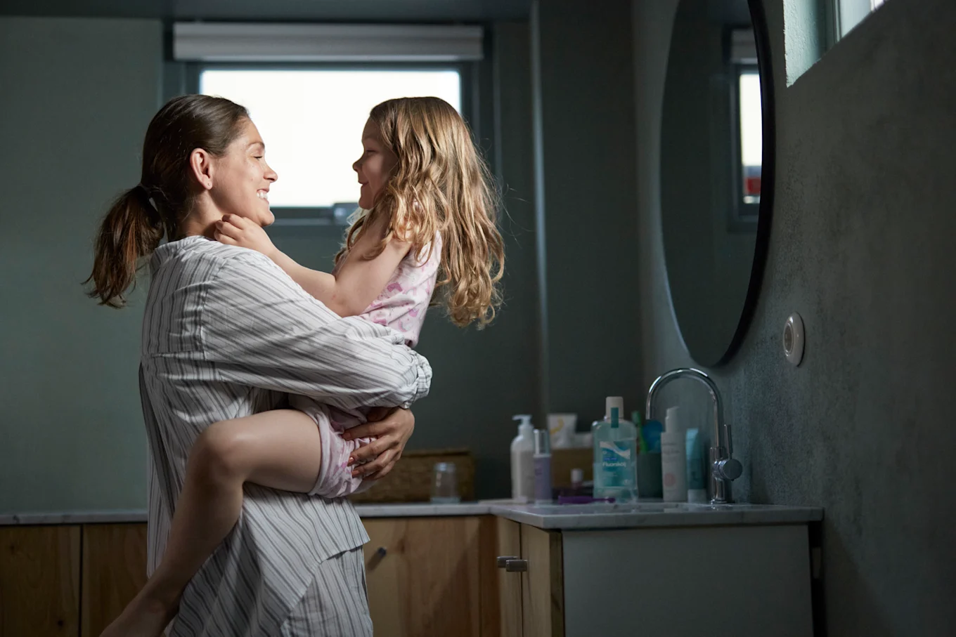 Mamma och dotter är i badrummet. Mamma håller sin dotter i famnen och båda skrattar.