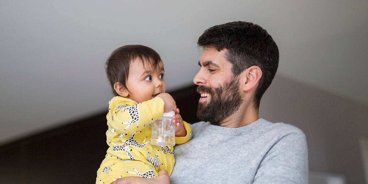 Pappa håller i bebis. De kollar på varandra med glädje. 