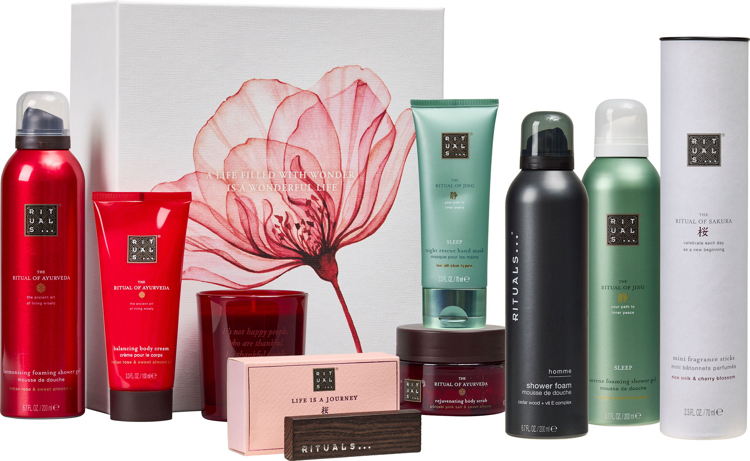 Flera Rituals-produkter står uppradade framför en vit presentask med rosa blomma, inklusive duschskum, kroppskräm, handmask och doftljus.