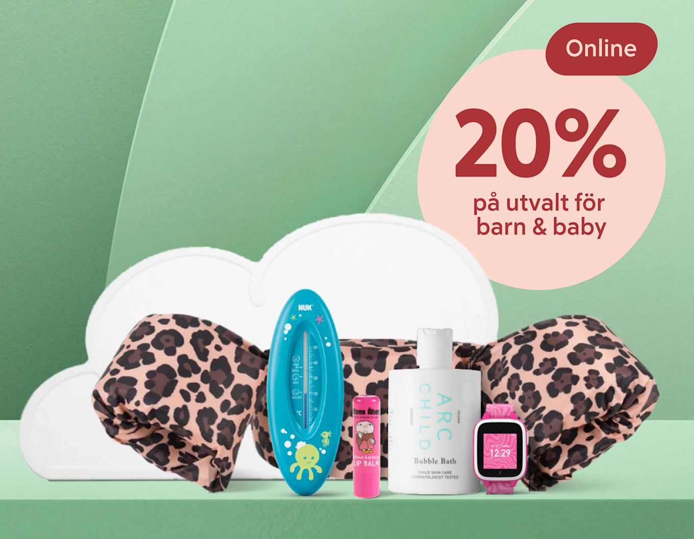 Barn- och babyprodukter som badtermometer, läppbalsam, badskum och rosa barnklocka visas framför en leopardmönstrad kudde.