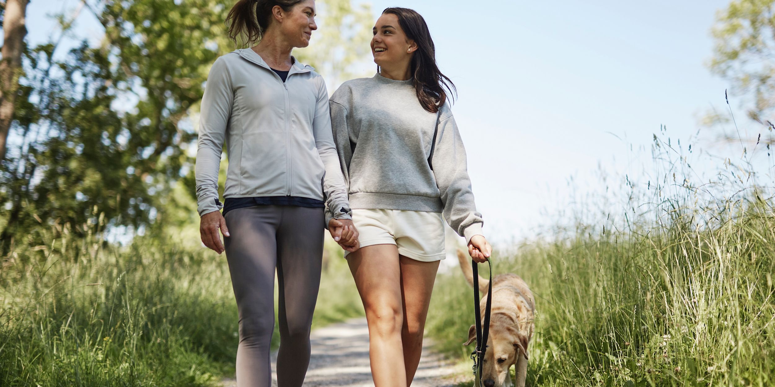 Tonårsdotter och mamma är ute och går på en promenad utomhus och pratar glatt med varandra.