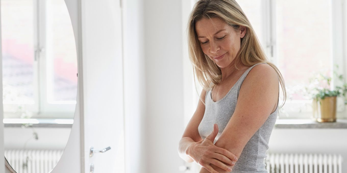 Kvinna står framför spegel och smörjer in sin arm.