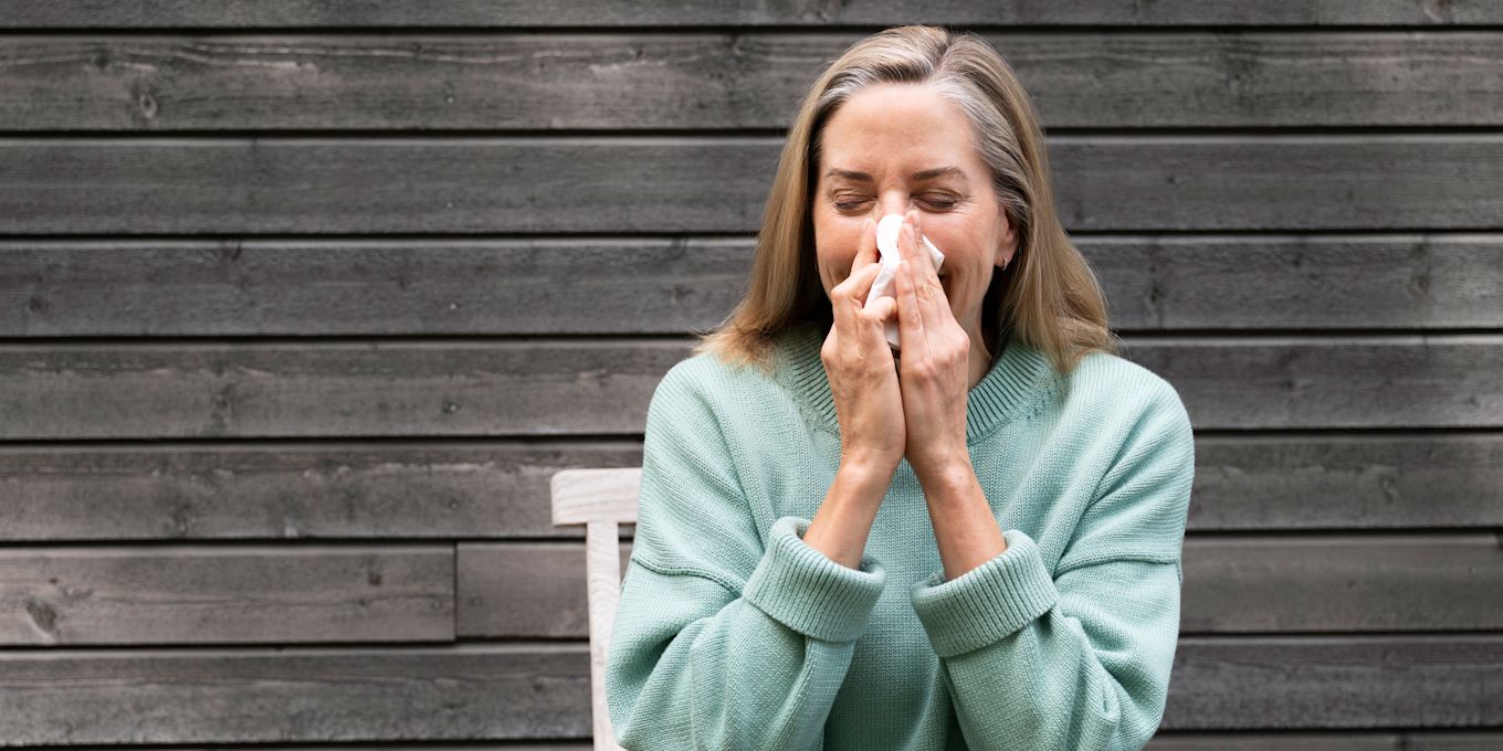 Kvinna sitter ute i solen och snyter sig.