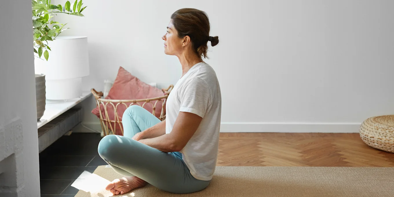 Kvinna sitter på en yogamatta och tittar ut genom fönstret.