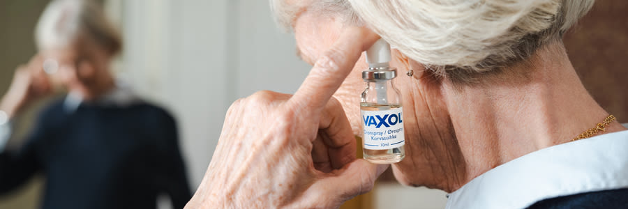 Äldre kvinna applicerar Vaxol öronspray i sitt öra i ett hemmiljö.