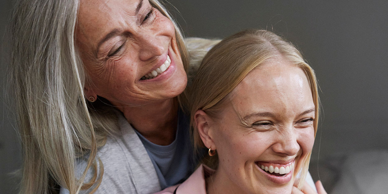 Kvinna håller om yngre tjej. Båda ler.