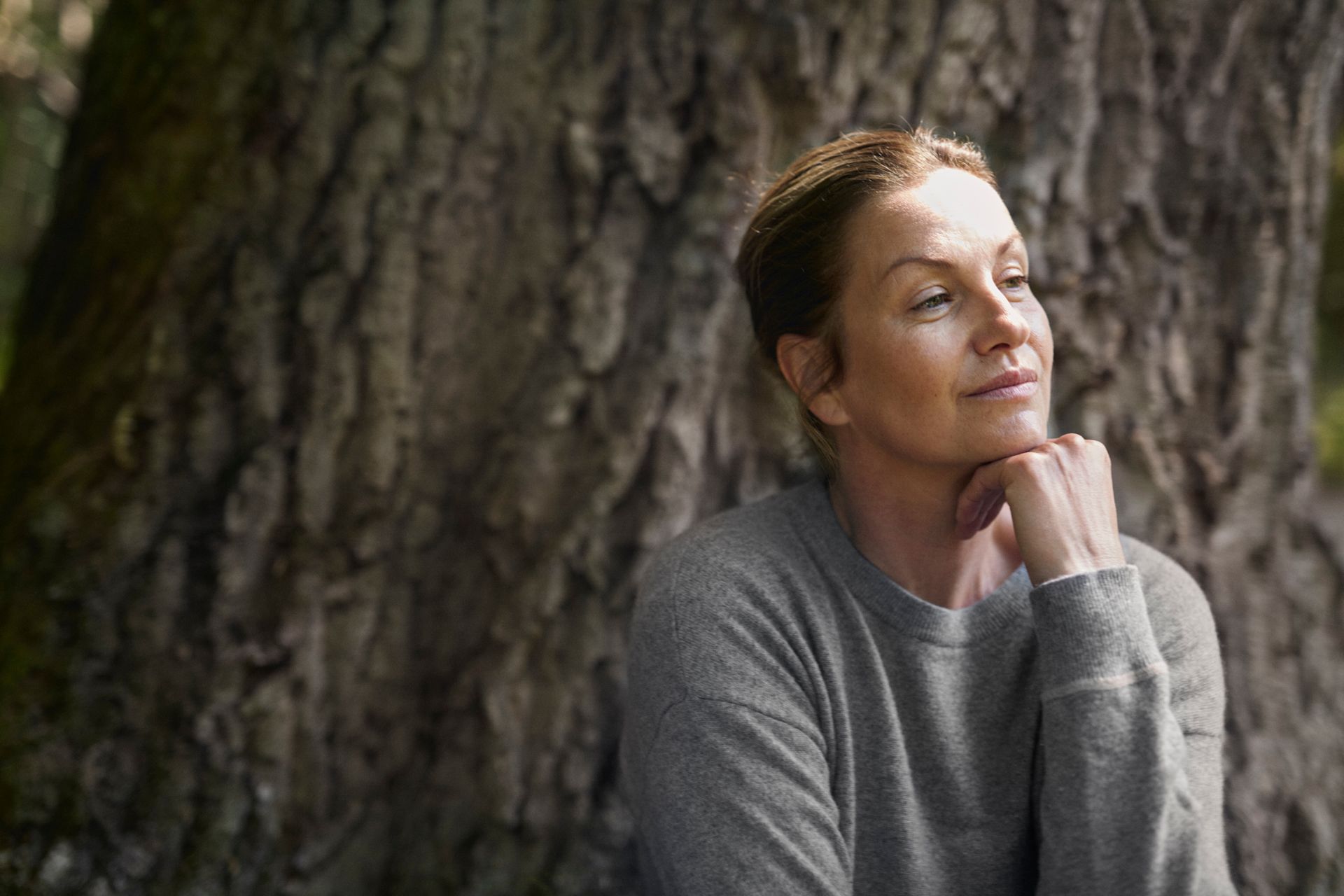 Kvinna sitter ute i naturen och tittar fundersamt åt sidan.