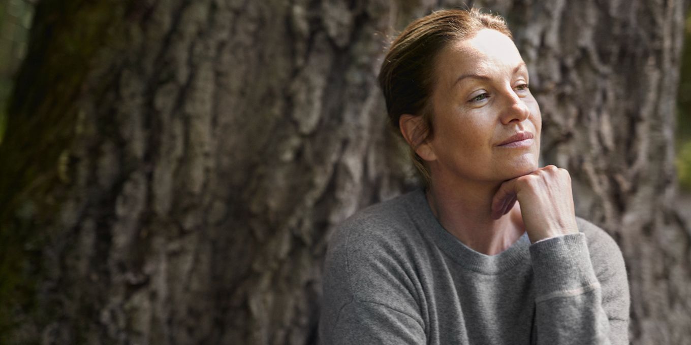 Kvinna sitter ute i naturen och tittar fundersamt åt sidan.