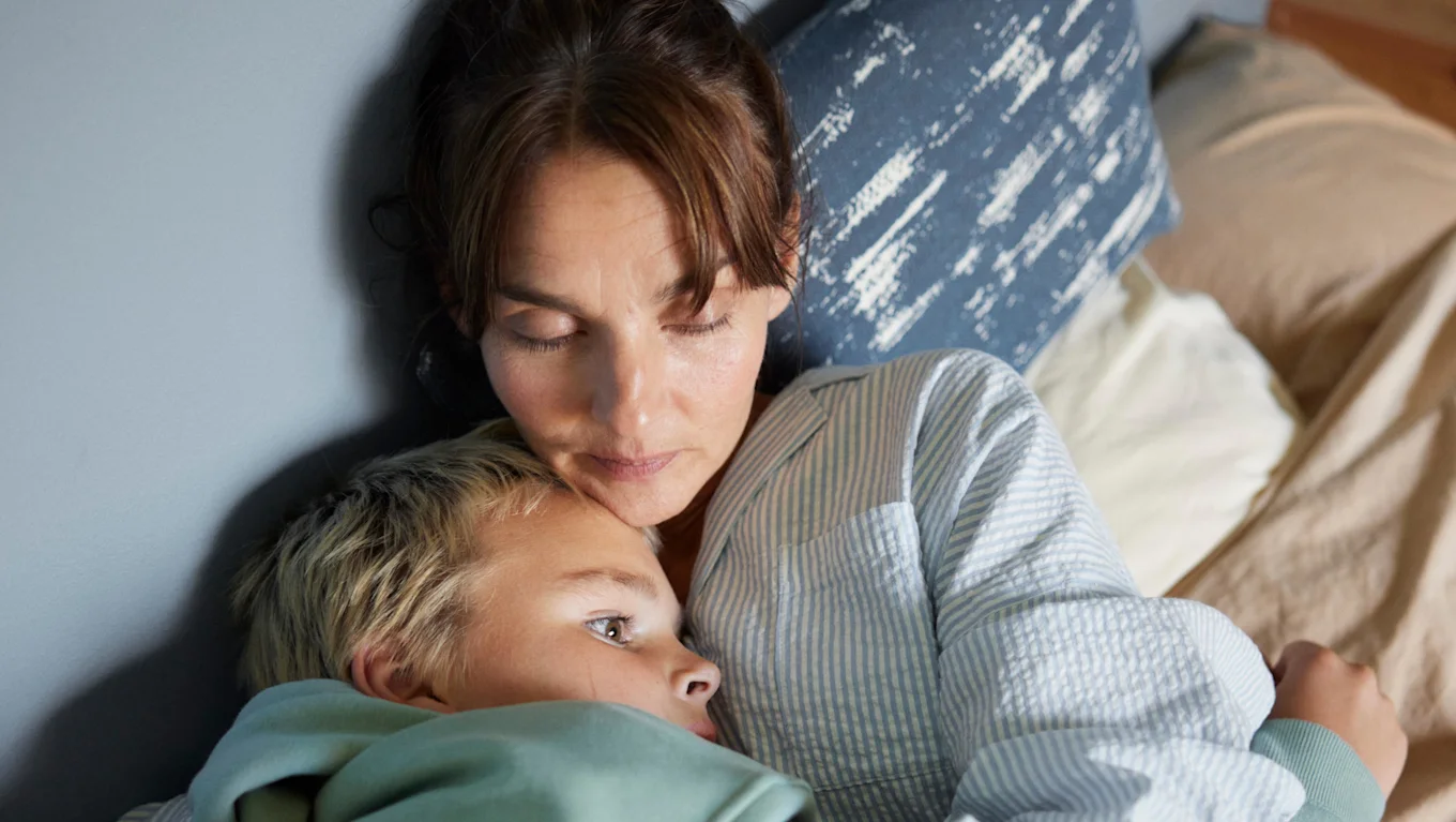 Mamma ligger och håller om sin son i sängen.